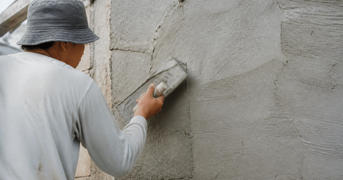 Ouvrier appliquant mortier gris sur mur vertical avec spatule