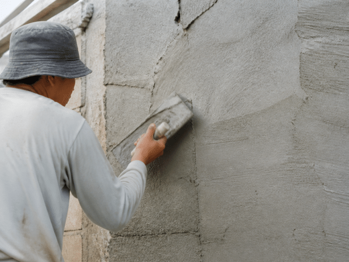 Ouvrier appliquant mortier gris sur mur vertical avec spatule
