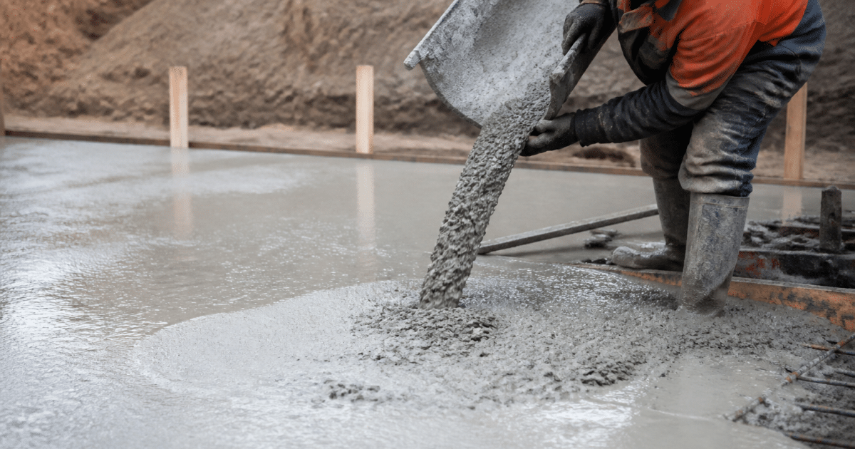 Ouvrier versant beton gris sur surface plane de fondation