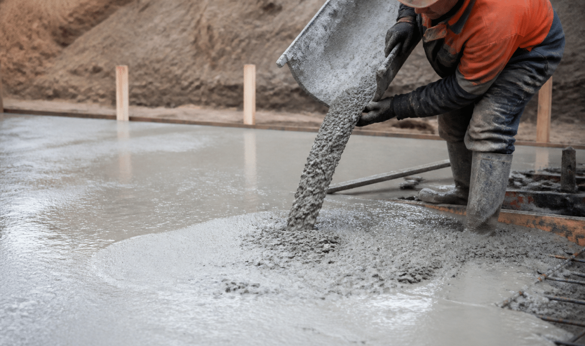 Ouvrier versant beton gris sur surface plane de fondation