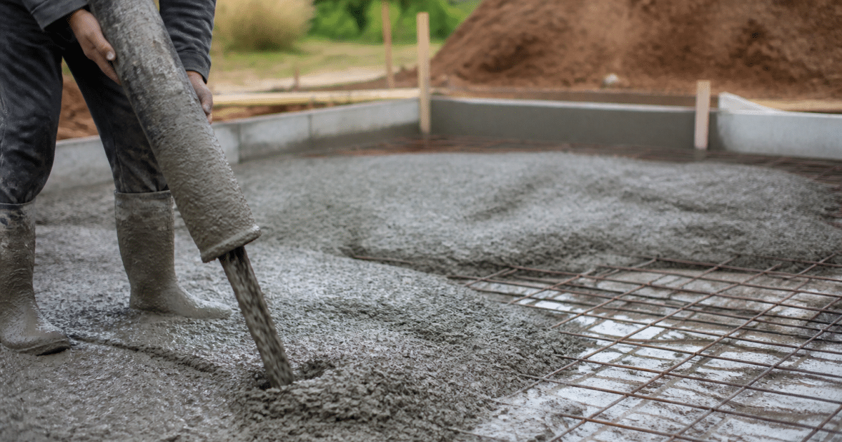 Ouvrier versant beton gris sur sol prepare pour fondation
