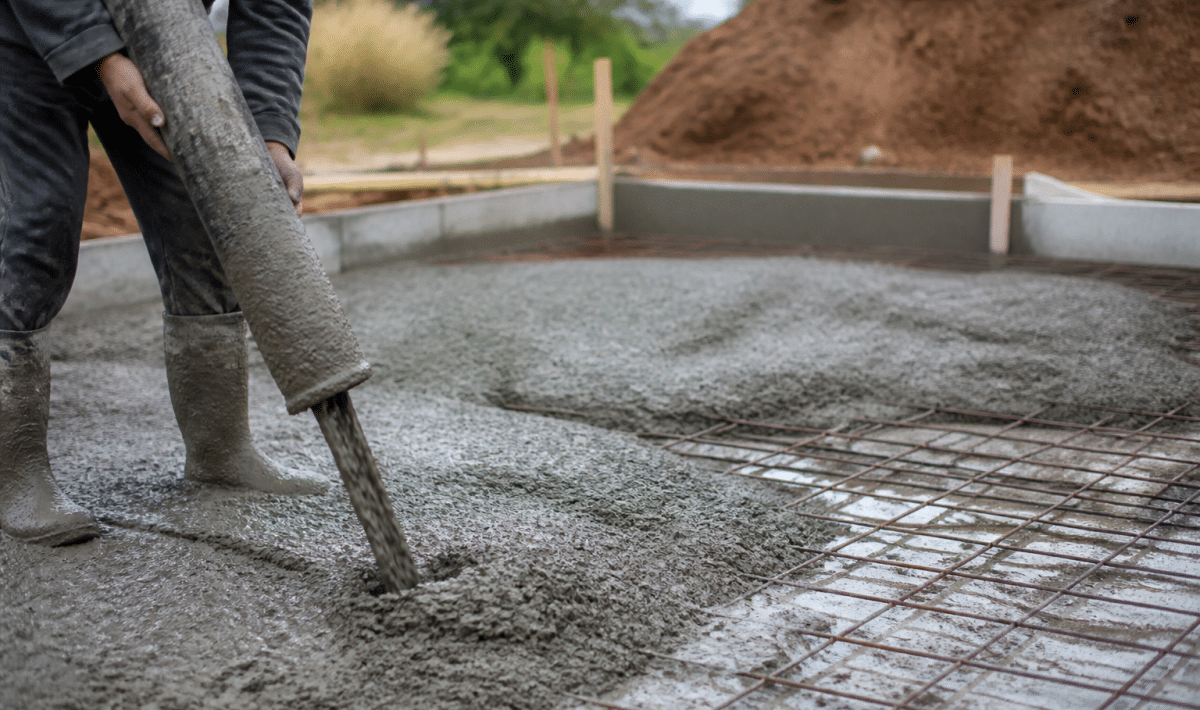 Ouvrier versant beton gris sur sol prepare pour fondation