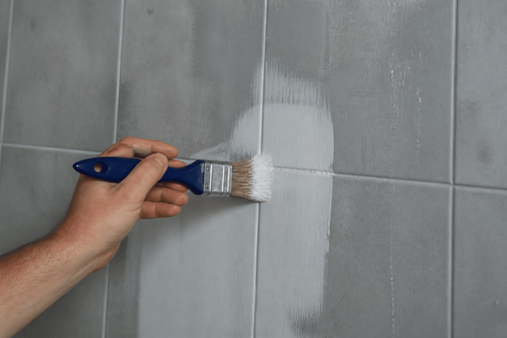 Pinceau appliquant enduit blanc sur surface carrelée humide