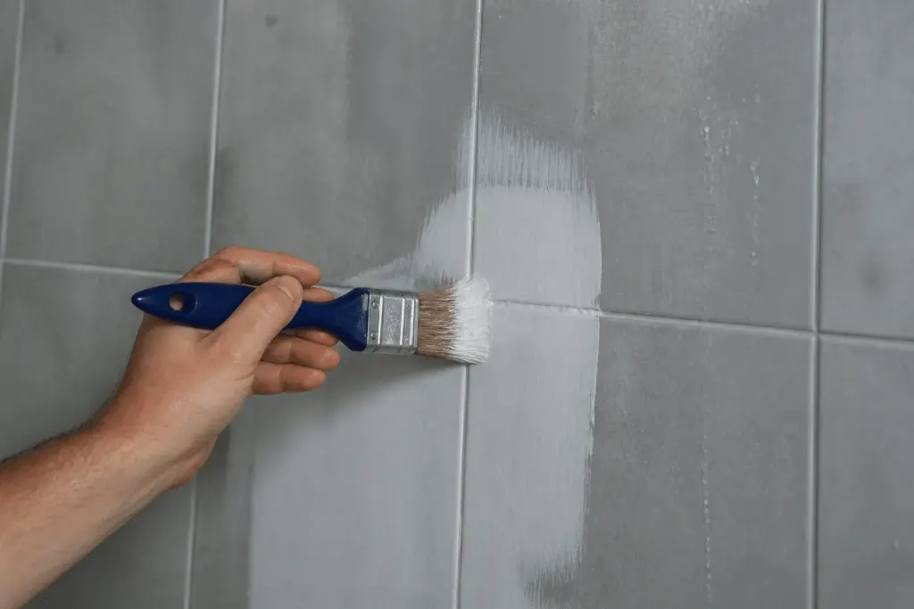 Pinceau appliquant enduit blanc sur surface carrelée humide