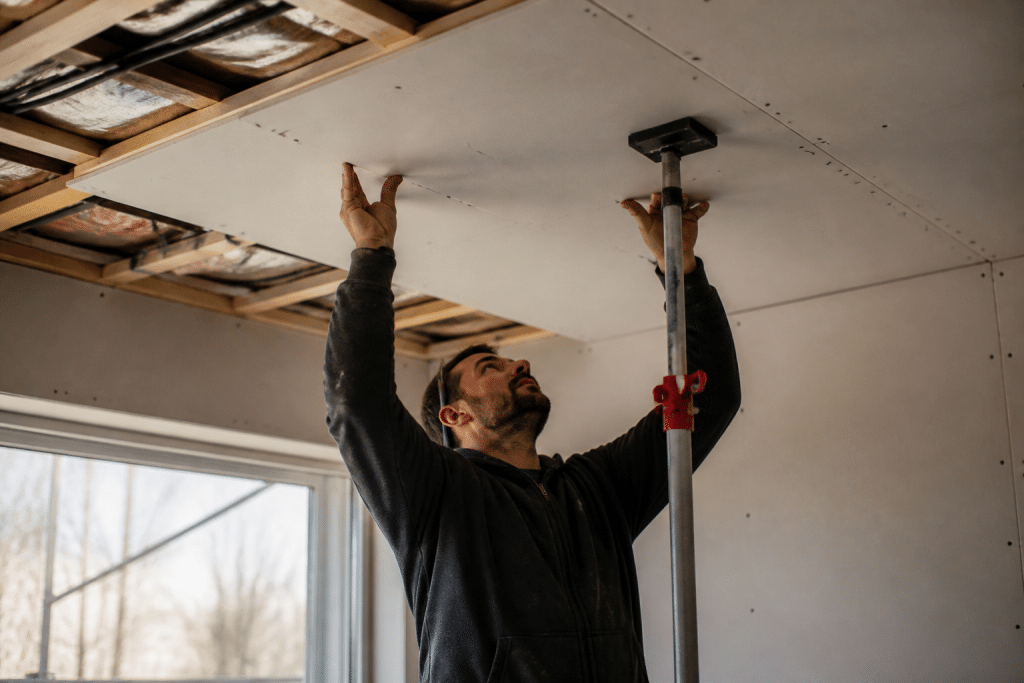 Ouvrier fixant plaque placo au plafond avec etai telescopique