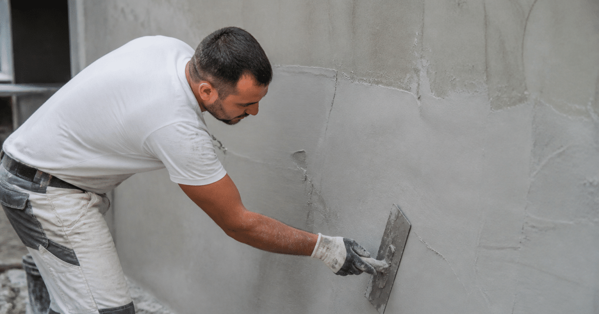 Ouvrier appliquant enduit lissant sur surface beton avec spatule large