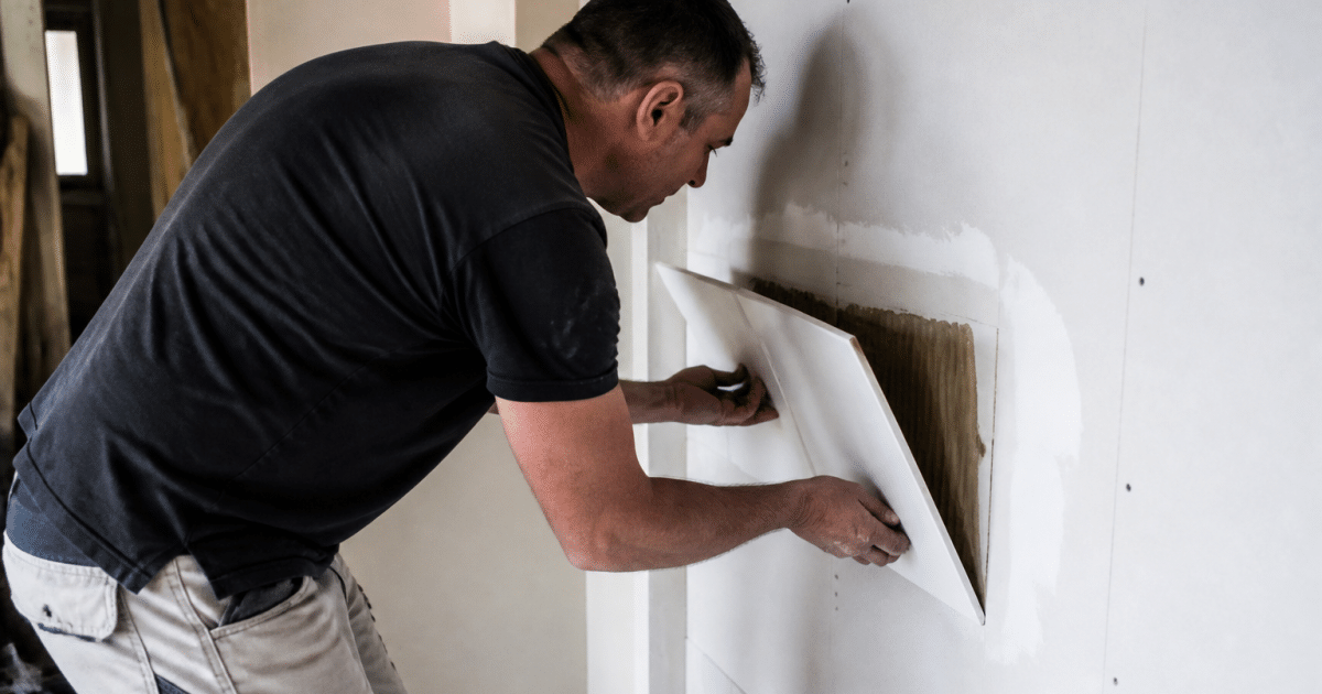 Ouvrier soulevant carrelage colle sur paroi placo blanc