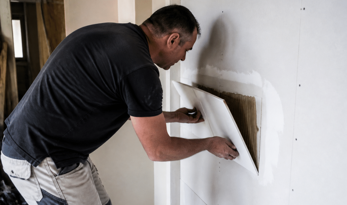 Ouvrier soulevant carrelage colle sur paroi placo blanc