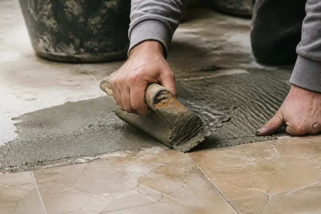 Mains appliquant materiau gris sur carrelage inegal