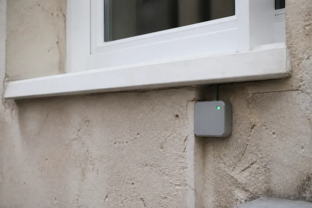 Petit boitier gris voyant vert sous fenetre blanche